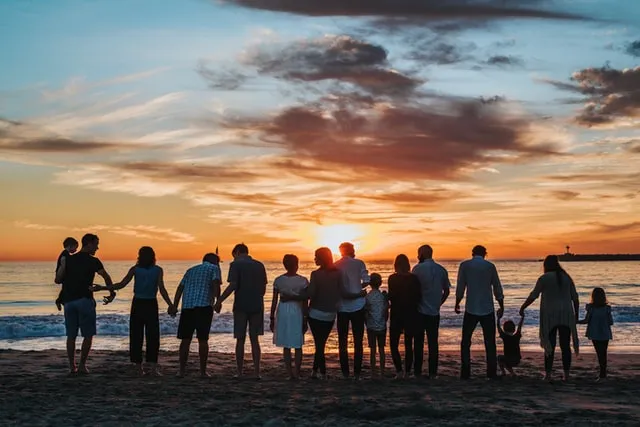 Wir sehen hier ein Bild mit einer Familie, die symbolisch für das Bild der Seelenfamilie stehen. Sie stehen Hand in Hand am Strand und schauen auf das Meer.