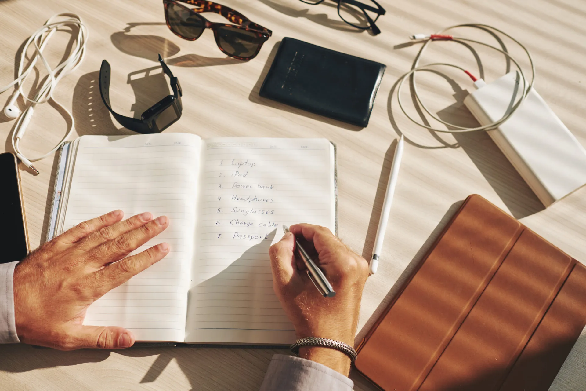 unrecognizable-man-writing-plan-journal-gadgets-lying-around-desk-scaled