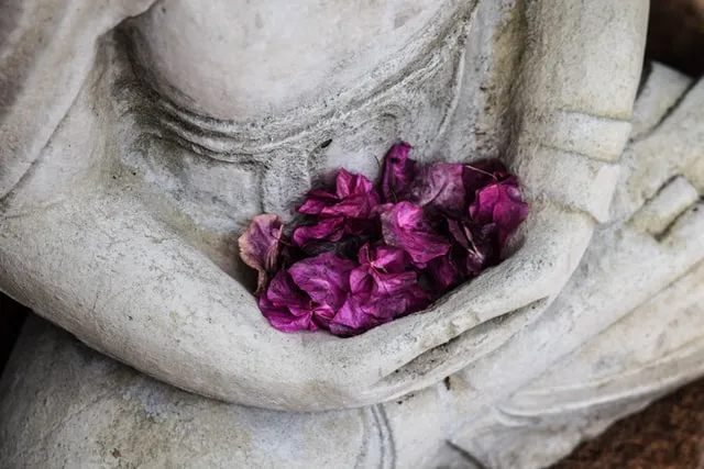 Bild zeigt eine Buddhastatue mit Blüten im Bereich des Sakralchakras - Samadhi / Erleuchtung durch Sexualität, Meditation und Tantra