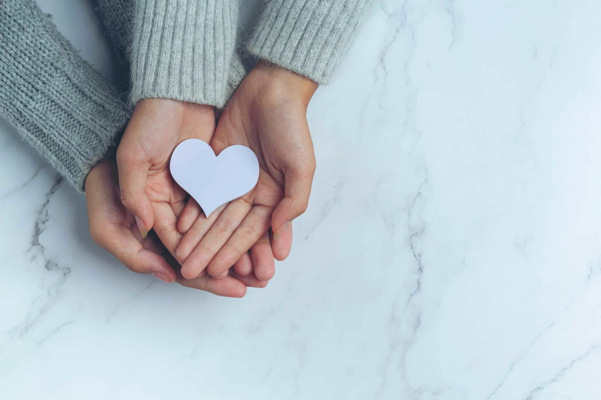 paper-heart-put-in-couple-s-hands-on-marble-table-scaled